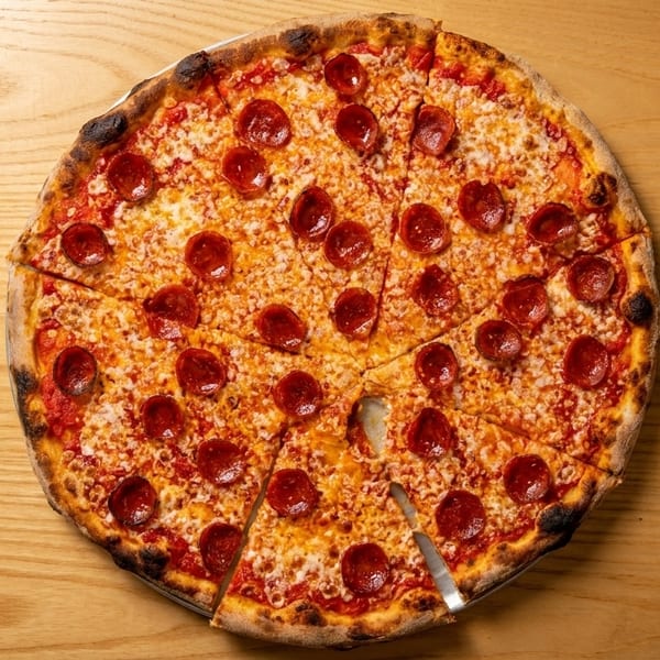 A whole pepperoni pizza with one slice removed, on a light wooden table.
