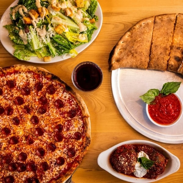 Table spread with pepperoni pizza, calzone, Caesar salad, meatballs, and a drink.